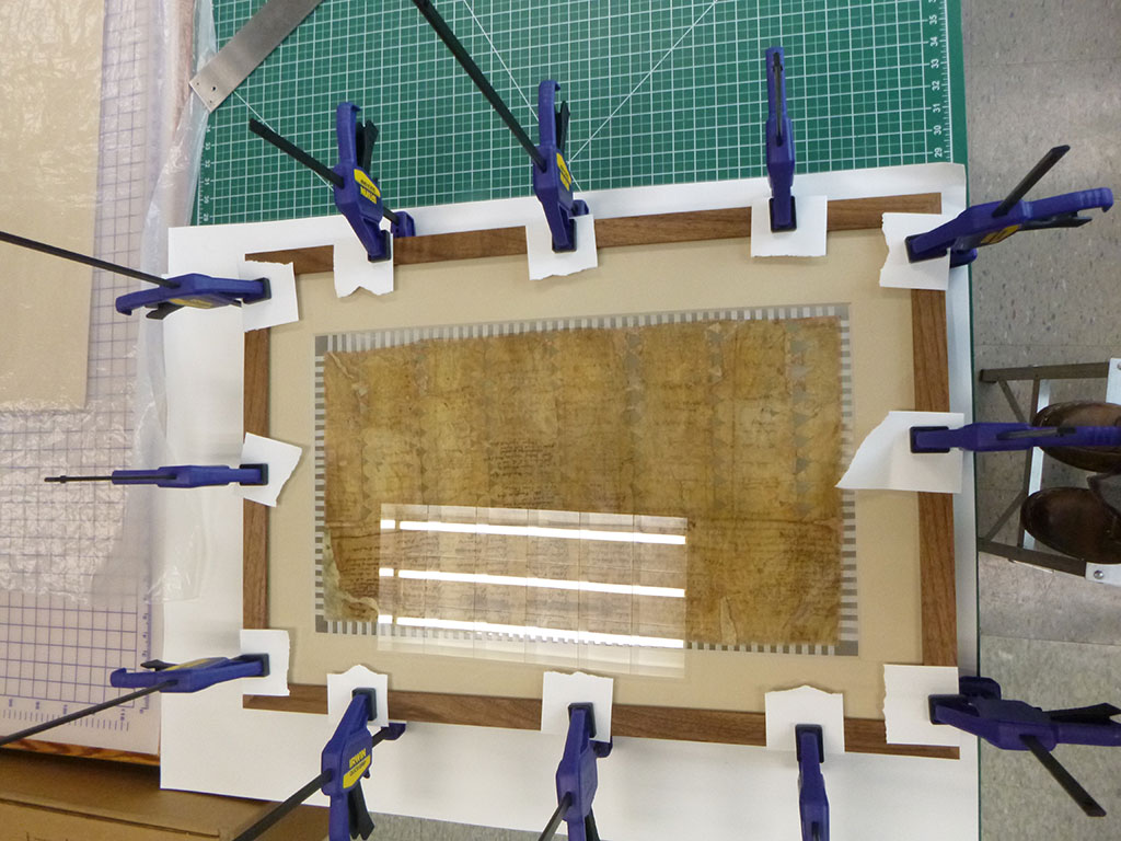 Sealing of double-sided frame from the verso with adhesive, barrier board, and clamps