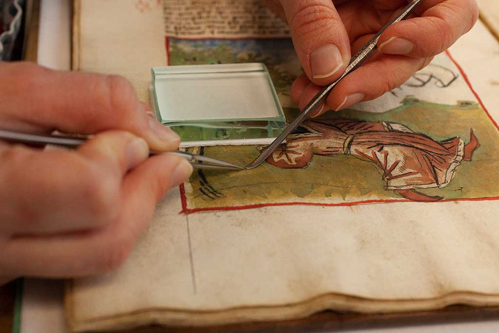 Applying the wheat starch paste and kozo fiber to a cracked area of the page. Previous repairs were dried under light pressure using a glass weight, blotter, and Hollytex.