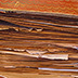 Detail of a scrapbook with brittle support pages. Brittle and loose fragments protrude beyond the text block—envelopes, folded newspapers, pamphlets, and a ribbon.